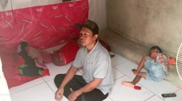 Arif duduk di dalam ruangan 3x3 meter berdinding bilik bambu yang ditinggalinya bersama istri dan dua anak. Rumah sempit ini menjadi tempat mereka bertahan hidup di tengah keterbatasan ekonomi